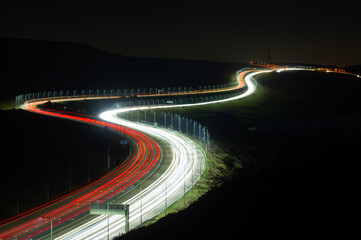 Long exposure light trails from traffic on a winding road at rush hour. Photograph of the UK M62 motorway taken from Scammonden bridge looking towards the summit. Traffic, travel or commute concept