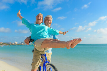 Happy senior couple exercising with bicycles on the beach on a sunny day