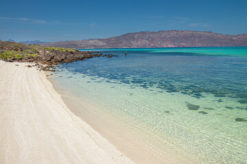 Obraz premium A beach with calm crystal clear water and white sands in the state of Baja California Sur. Mexico with mountains in the background. Loreto, Coronado island or isla coronado.