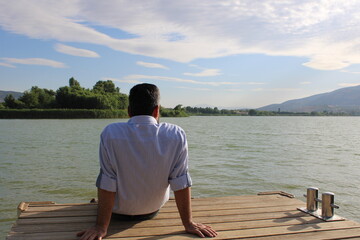 Fototapeta na wymiar man sitting on the pier against the lake. man watching the lake on the dock