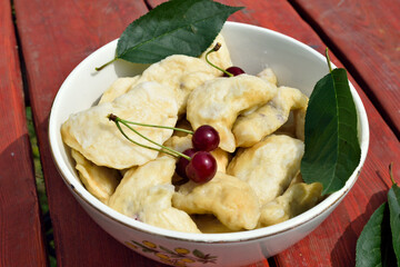 dumplings with cherries on a wooden table in the yard, close-up