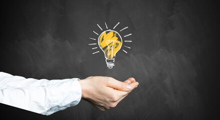 female hands with a lightbulb symbol in front of a chalkboard