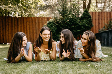 Four women best friends lying on grass, having good time, chatting and laughing.