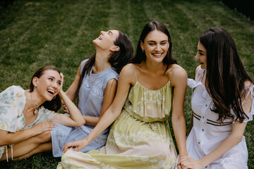 Four friends, young women, sitting in a park on green grass, having good time.