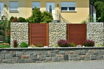 Moderner Sichtschutzzaun abwechselnd aus mit Naturstein gefüllten Gabionen aus verzinktem Stahlgitter und lasierter Holzbretterverschalung um ein bebautes Grundstück © Hermann