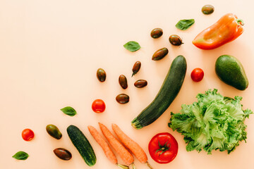 Zucchini, avocado, tomato, carrot, cucumber, bell peper and lettuce on beige background. Healthy raw vegan food, diet, detox concept. Top view, flat lay, copy space