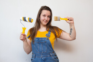 woman chooses between roller and brush on background ladder and gray cement wall. choice of tools for painting and priming. beginner in renovation