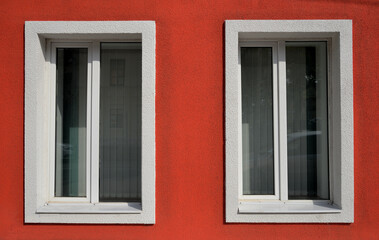 Fototapeta na wymiar Red wall with two windows with shutters
