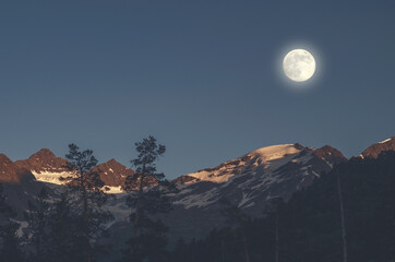Full moon in the mountains. The moon illuminates the snowy peaks of the mountains. Sunset in the highlands.