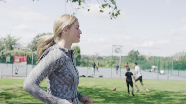 Side shot of young woman jogging through a park, in slow motion 