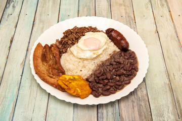Popular Colombian paisa tray from the Antioquia area with fried egg, banana, beans and white rice, chorizo and fried bacon on wooden table