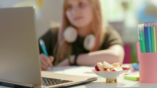 Closeup on smiling girl in grey shirt with laptop homeschooling and eating healthy snack at home in sunny day.