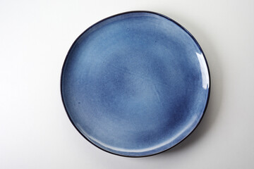 Top view of a new round blue ceramic plate with a black rim on white background