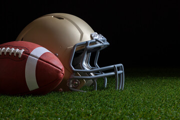 Low angle view of football and gold helmet on grass with dark background © Daniel Thornberg
