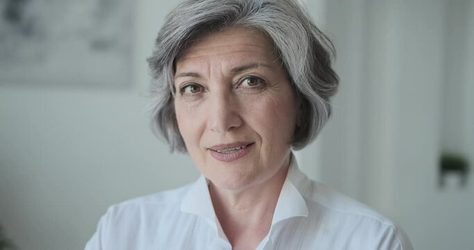 Headshot smiling and gazing at the camera, a gorgeous, confident older lady constructor smirks. A stylish senior female reporter or columnist standing in a bright studio.