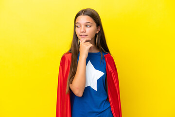 Little caucasian superhero girl isolated on yellow background looking to the side