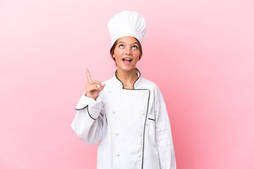 Little caucasian chef girl isolated on pink background pointing up and surprised