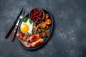 English breakfast with fried eggs, bacon, sausages, beans, toasts on black background