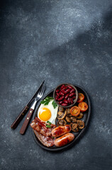 English breakfast with fried eggs, bacon, sausages, beans, toasts on black background