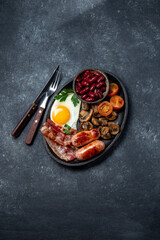 English breakfast with fried eggs, bacon, sausages, beans, toasts on black background