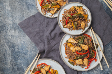 Japanese dish buckwheat soba noodles with chicken and vegetables carrot, bell pepper and green beans in wok on dark blue background
