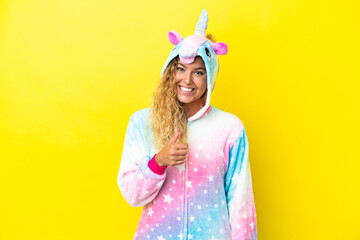 Girl with curly hair wearing a unicorn pajama isolated on yellow background giving a thumbs up gesture