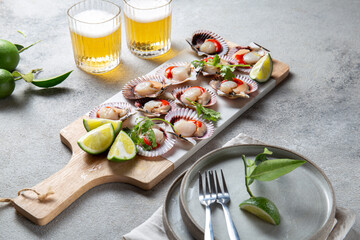 Raw Seafood shellfish scallops with lemon, cilantro and michelada beer drink on white board, gray background