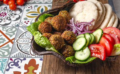 Falafel, fresh vegetables and pita bread on clay plate, gray background