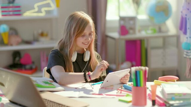smiling modern child in grey shirt with tablet PC and workbook learning online at home in sunny day.