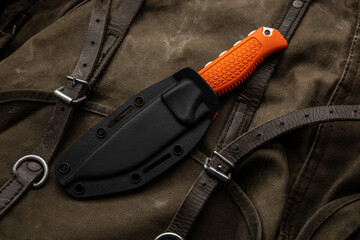 A hunting knife with a orange rubberized grip on a khaki canvas backpack. Weapons for self-defense...