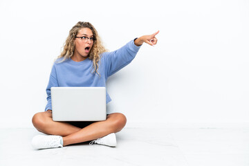 Naklejka premium Girl with curly hair with a laptop sitting on the floor pointing away