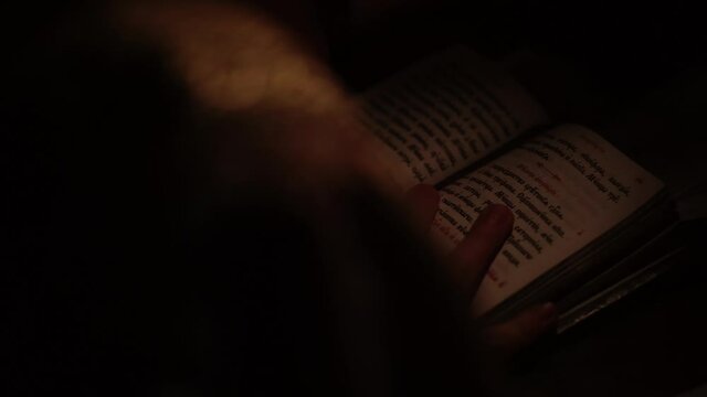 Religion, holidays, concept - close-up of children hands holding ancient book and reading following text with finger in dark room by light of candle. Church ministers perform divine services in church