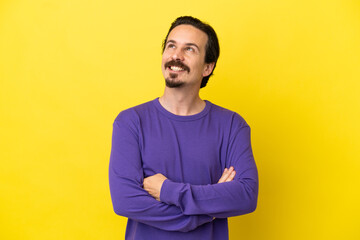 Young caucasian man isolated on yellow background looking up while smiling