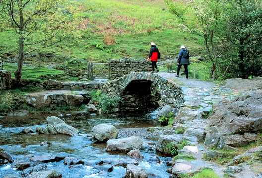 Lakes Region, England, Tourist hiking over a High Sweden Bridge which is a historic stone humpbacked packhorse bridge,