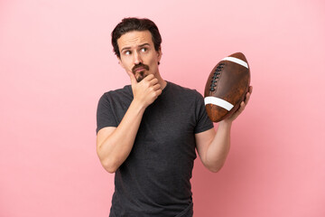 Young caucasian man playing rugby isolated on pink background having doubts