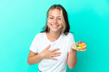 Young Russian woman holding a fruit sweet isolated on blue background smiling a lot