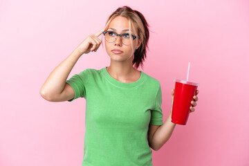 Young Russian woman holding a refreshment isolated on pink background having doubts and thinking