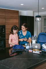 Mother explaining to her daughter how to prepare an emergency backpack in the kitchen