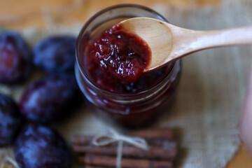 Wooden spoon with plum jam in a glass jar. Healthy food background concept. Close up, selective focus and copy space