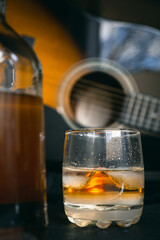 glass of whiskey with a guitar and a bottle in the background