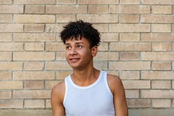 Afro latin male teenager smiling against a wall