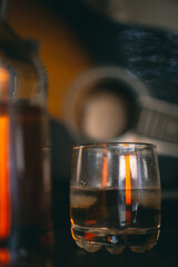 glass of whiskey with a guitar and a bottle in the background