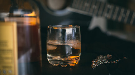 glass of whiskey with a guitar and a bottle in the background