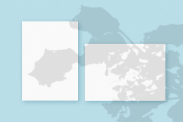 Mockup with plant shadows superimposed on an horizontal and vertical sheet of textured white paper on a blue table background