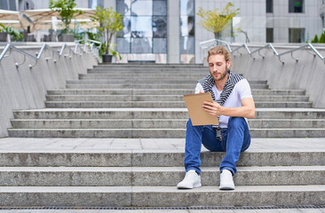An attractive man with a sketchbook sits on the steps.
