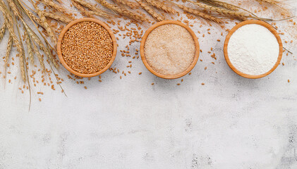 Fototapeta na wymiar Wheat grains , brown wheat flour and white wheat flour in wooden bowl set up on white concrete background.