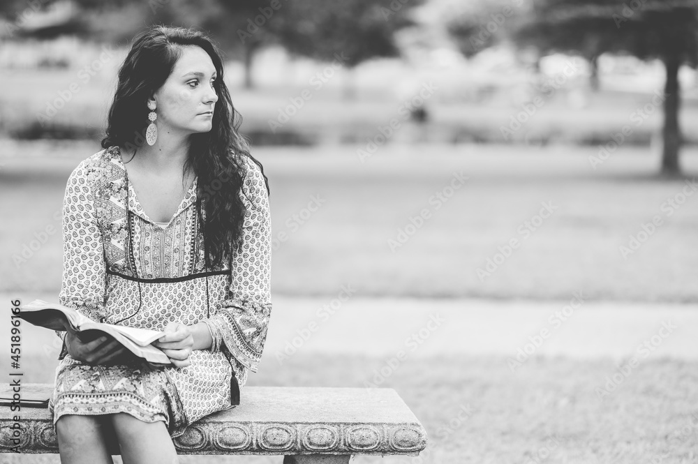 Poster Young Caucasian woman reading the Bible while sitting on a bench