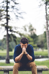 Young Caucasian man praying while sitting on a bench