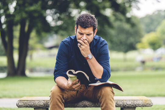Young Caucasian man reading the Bible while sitting on a bench