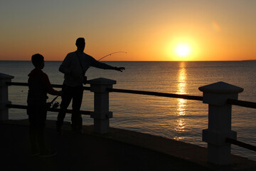 father and son fishing on the pier at sunset